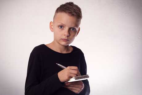 Junge mit Rechenschwäche schaut verängstigt und schreibt in Notizblock