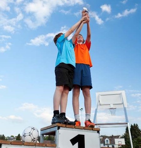 Kinder mit Pokal bei Wettbwerb auf dem Siegertreppchen