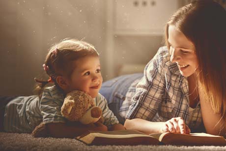 Erziehungsratgeber stellen Eltern-Kind-Beziehung ins Zentrum:Mutter und Tochter beim Buch vorlesen und lächeln