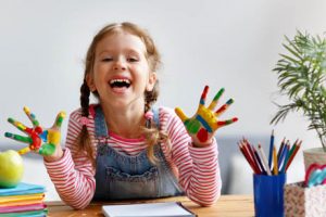 Kreativität bei Kindern fördern - Mädchen mit bunter Farbe an den Händen lacht