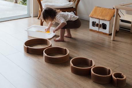 Montessorimaterial Ein Kind spielt versonnen mit Ringen aus Holz und schüttet